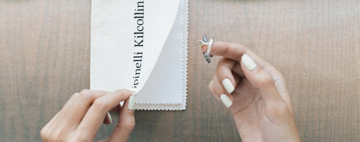 Hands cleaning a ring with a Spinelli Kilcollin polishing cloth